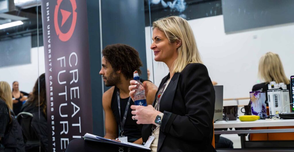 A Performers College careers manager speaking with a student at a Creative Futures careers session, beside a BIMM University Careers Department banner