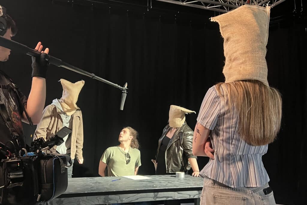 Performers College acting students filming a scene with three actors wearing hessian sacks over their heads, watched by a camera and boom operator