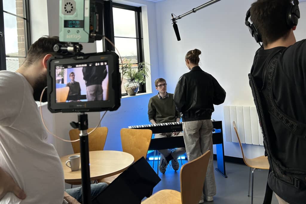 Performers College acting students filming a scene, with a camera operator and boom operator capturing an actor at a keyboard