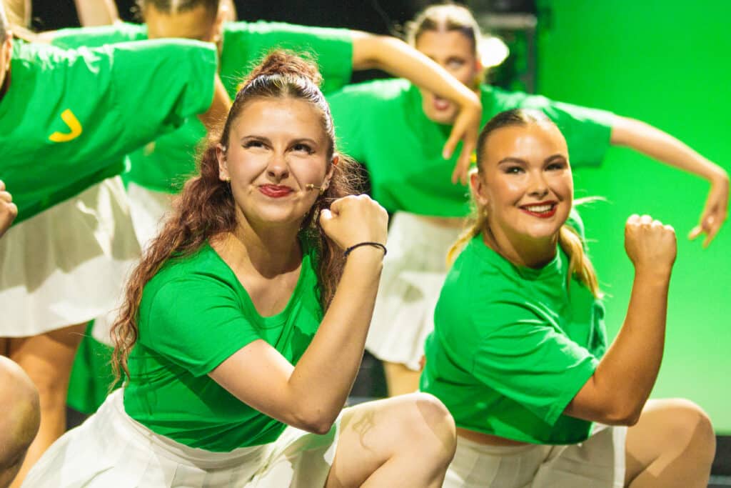 Performers College Birmingham performing arts students in green tops and white skirts dance energetically on stage during Pulse.